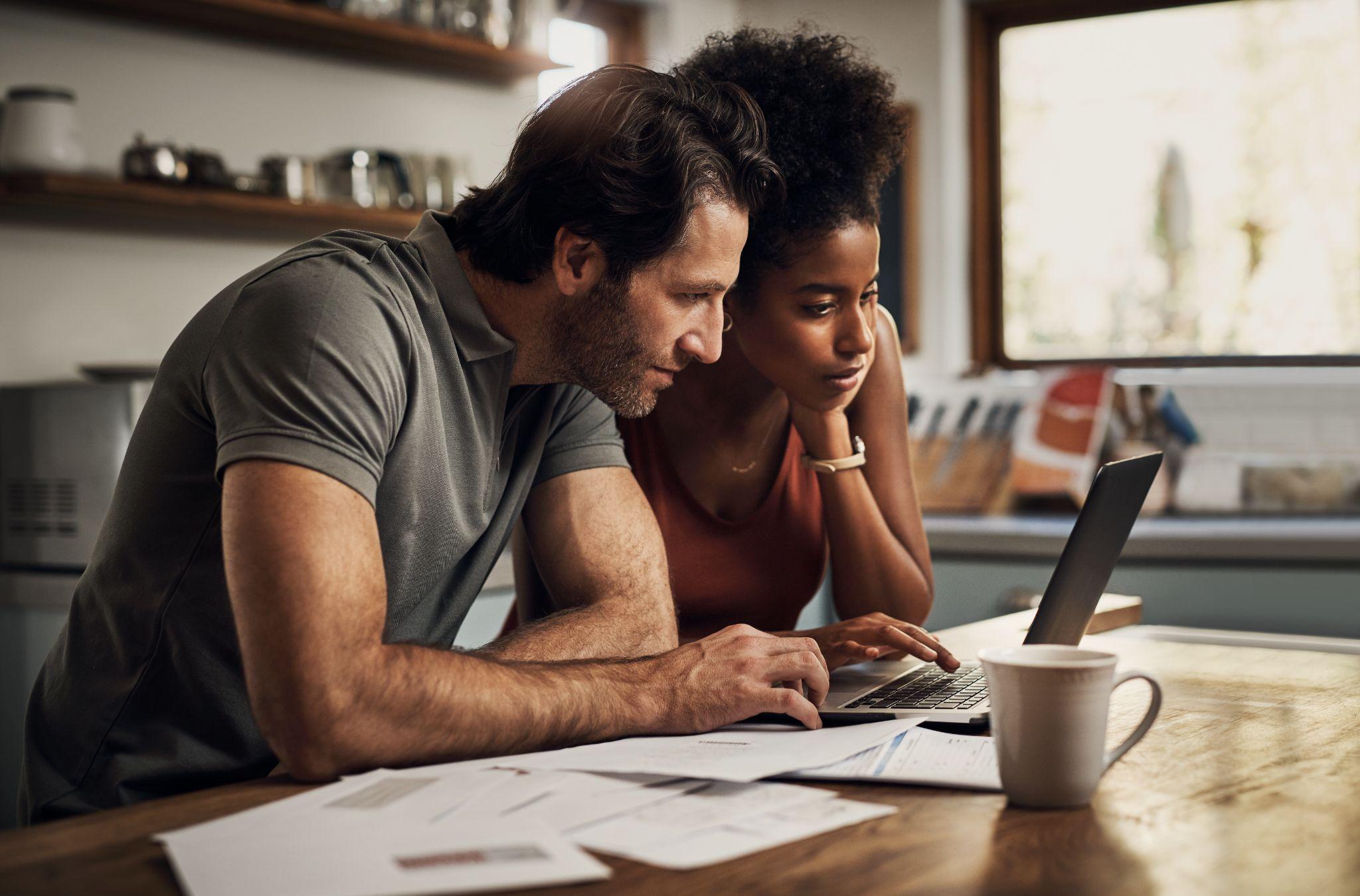 Couple with a laptop doing finance paper work, paying debt insurance loans or online ebanking together at home.