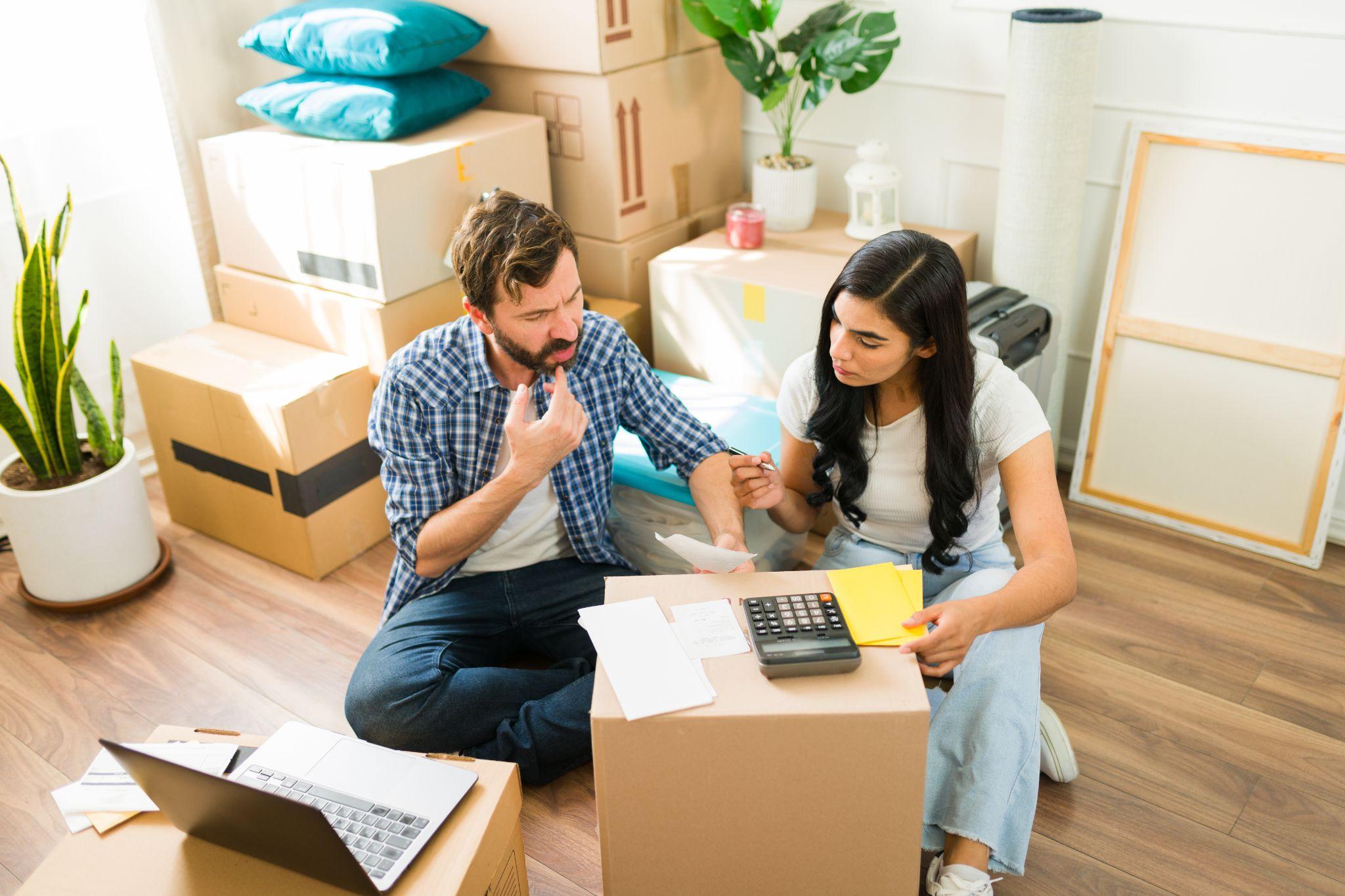 Young couple in their new apartment, sitting amidst cardboard boxes and budgeting for their move