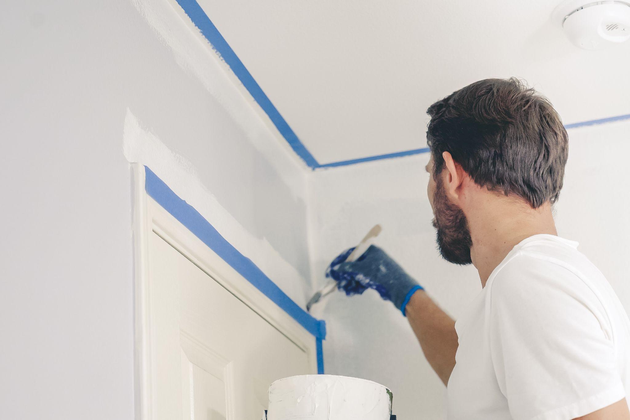 painter hands with gloves painting the wall edge by door frame.