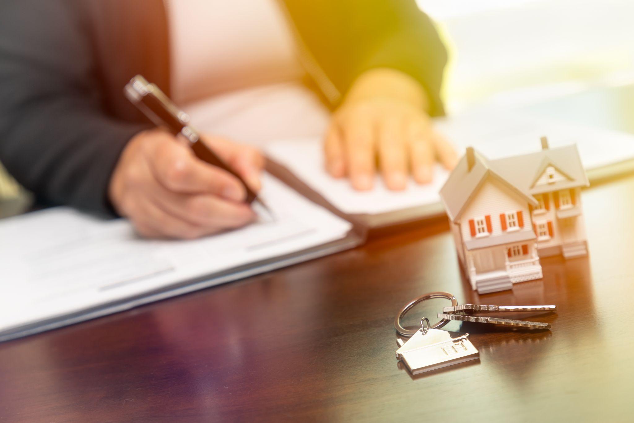 Woman signing real estate contract papers with house keys, home keychain and small model home in front